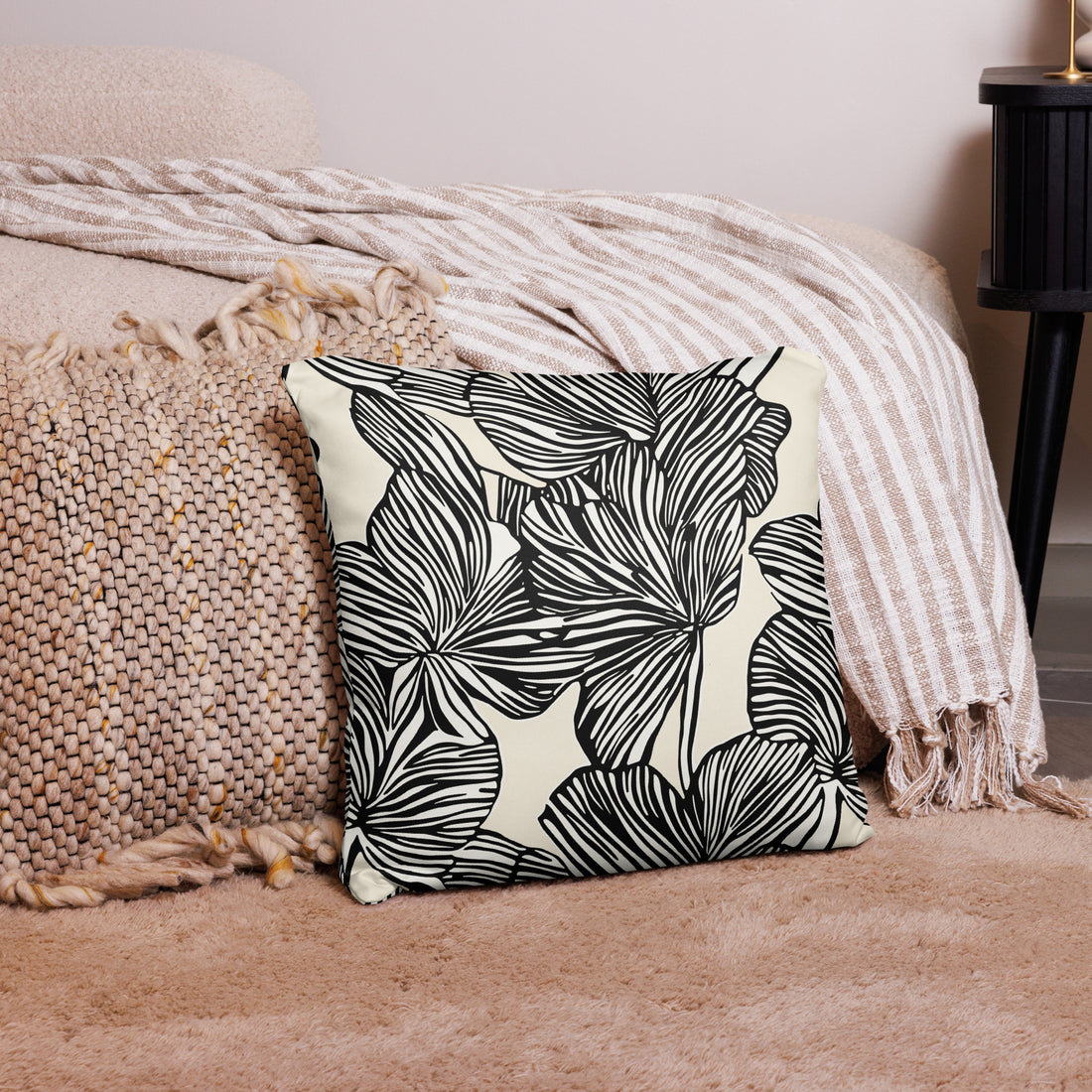 Monochrome pillow with black botanical leaf patterns on a beige background placed on a cozy beige knitted throw.