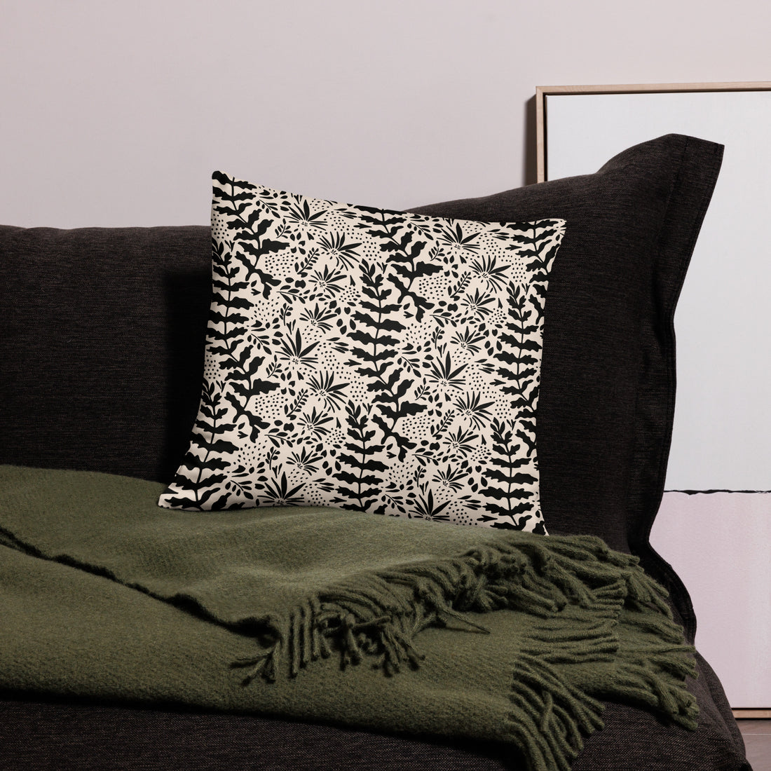 Monochrome knit pillow with black and white botanical design, placed on a dark sofa with a green throw.