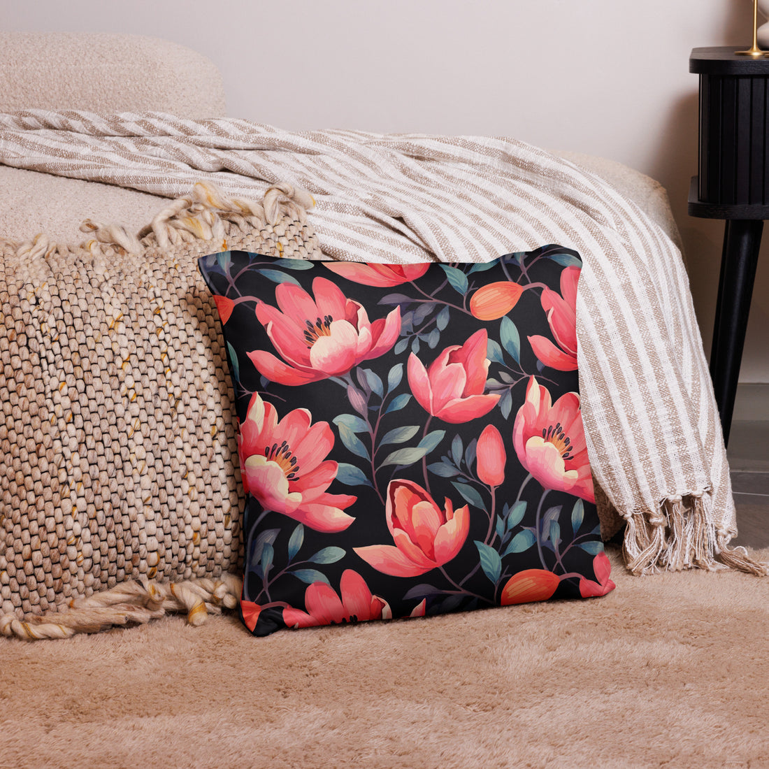 Decorative pillow featuring vibrant coral magnolia flowers on a black background, placed on a textured beige throw.