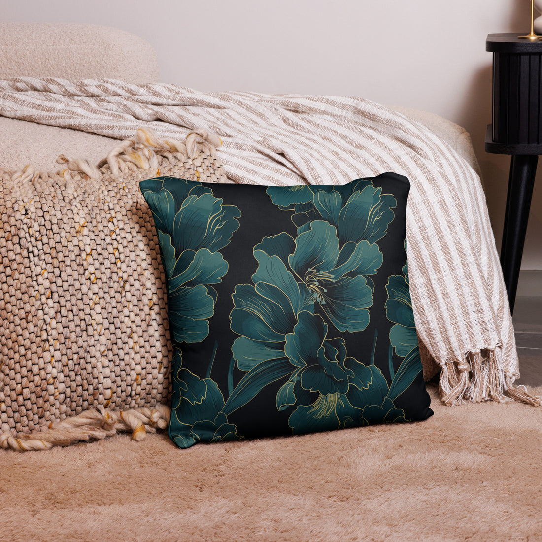 Square pillow with teal floral design on dark background, placed on cozy beige throw.