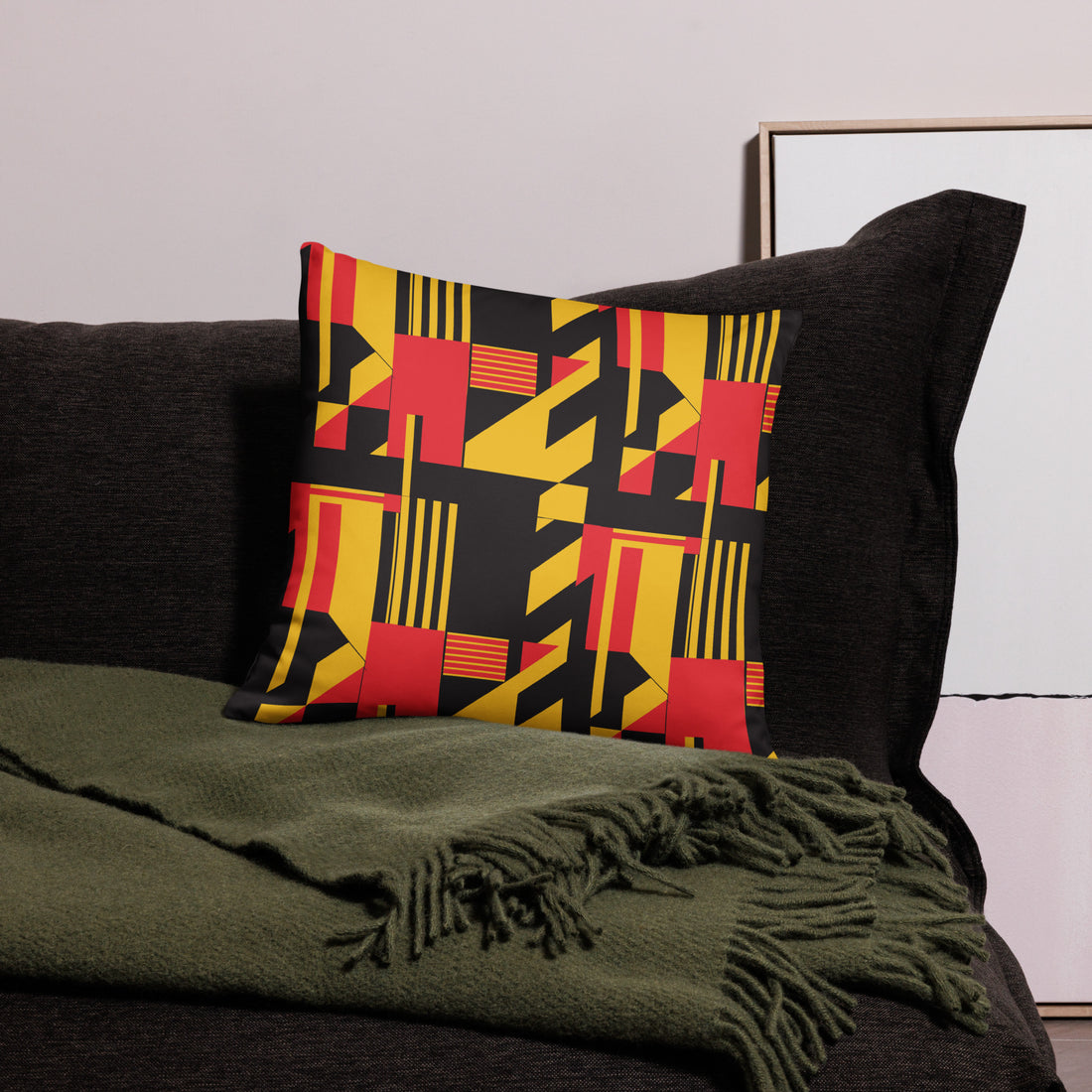 Pillow with bold geometric design in black, red, and yellow hues, set on a dark couch.