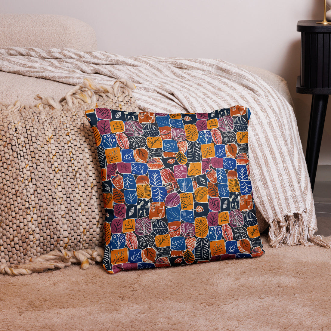 Pillow with autumnal leaf pattern in warm hues of rust, gold, and navy, displayed on a cozy beige surface.