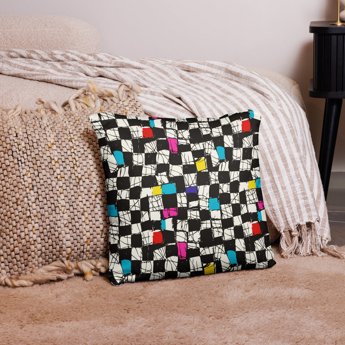 Colorful geometric patterned pillow with black, white, red, blue, and yellow blocks on a textured background.