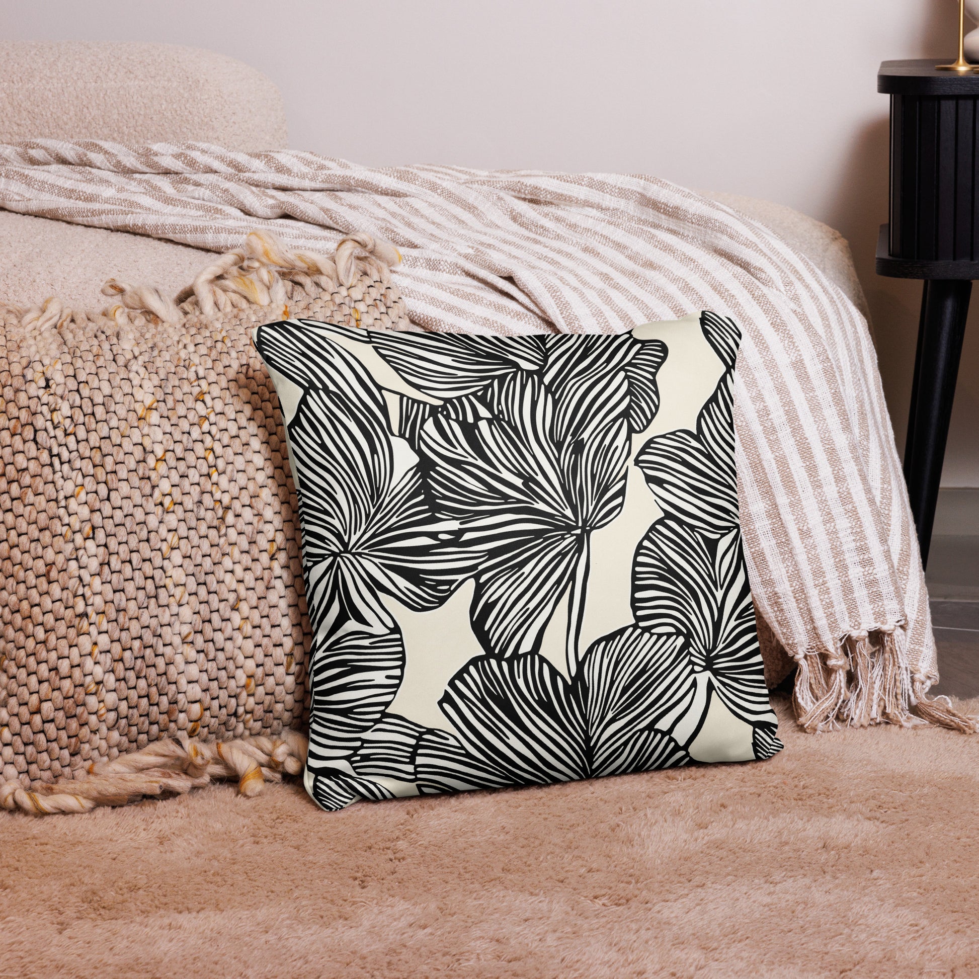 Monochrome pillow with black botanical leaf patterns on a beige background placed on a cozy beige knitted throw.