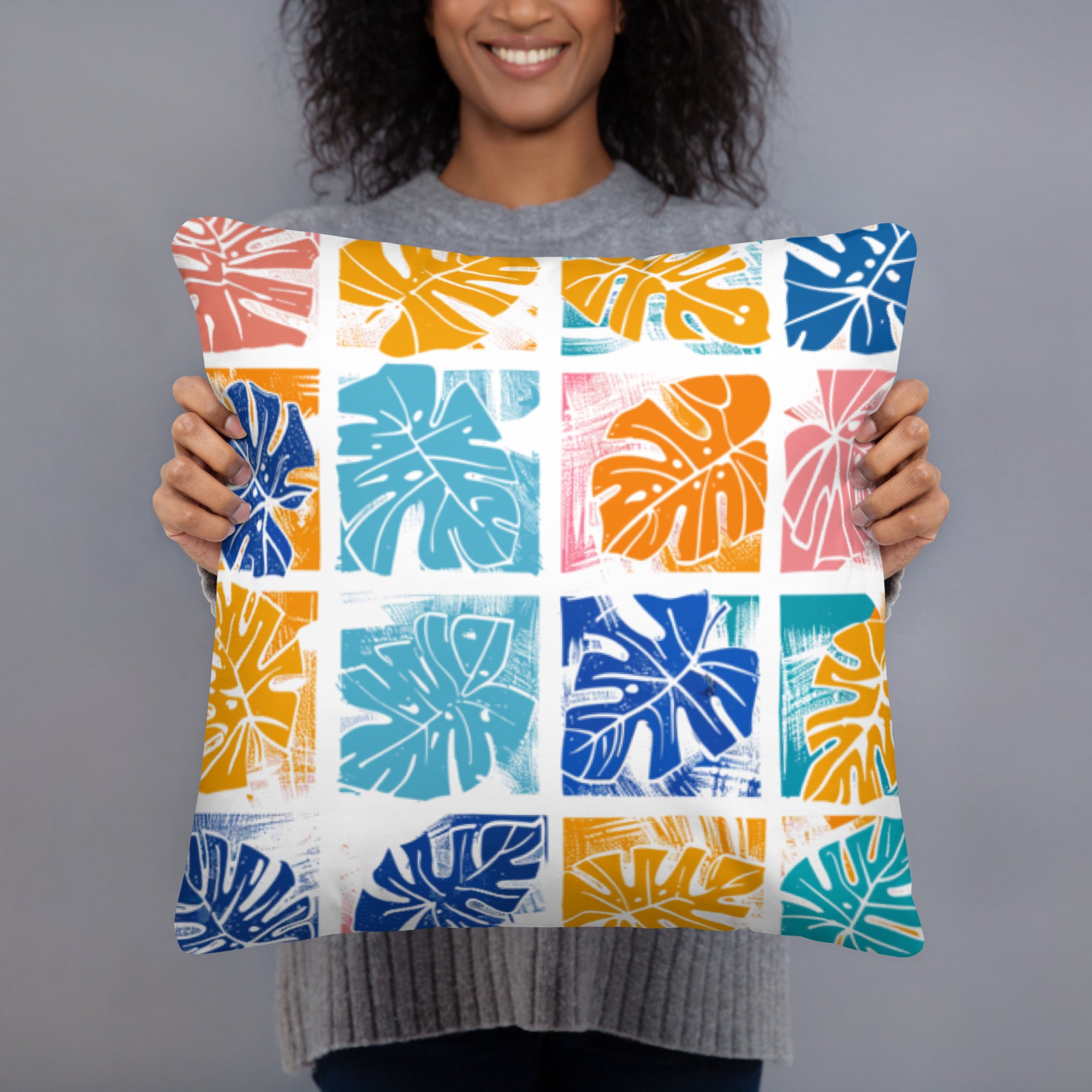 Close-up of a pillow with a colorful monstera leaf design featuring blue, orange, yellow, and pink colors on a knitted surface.