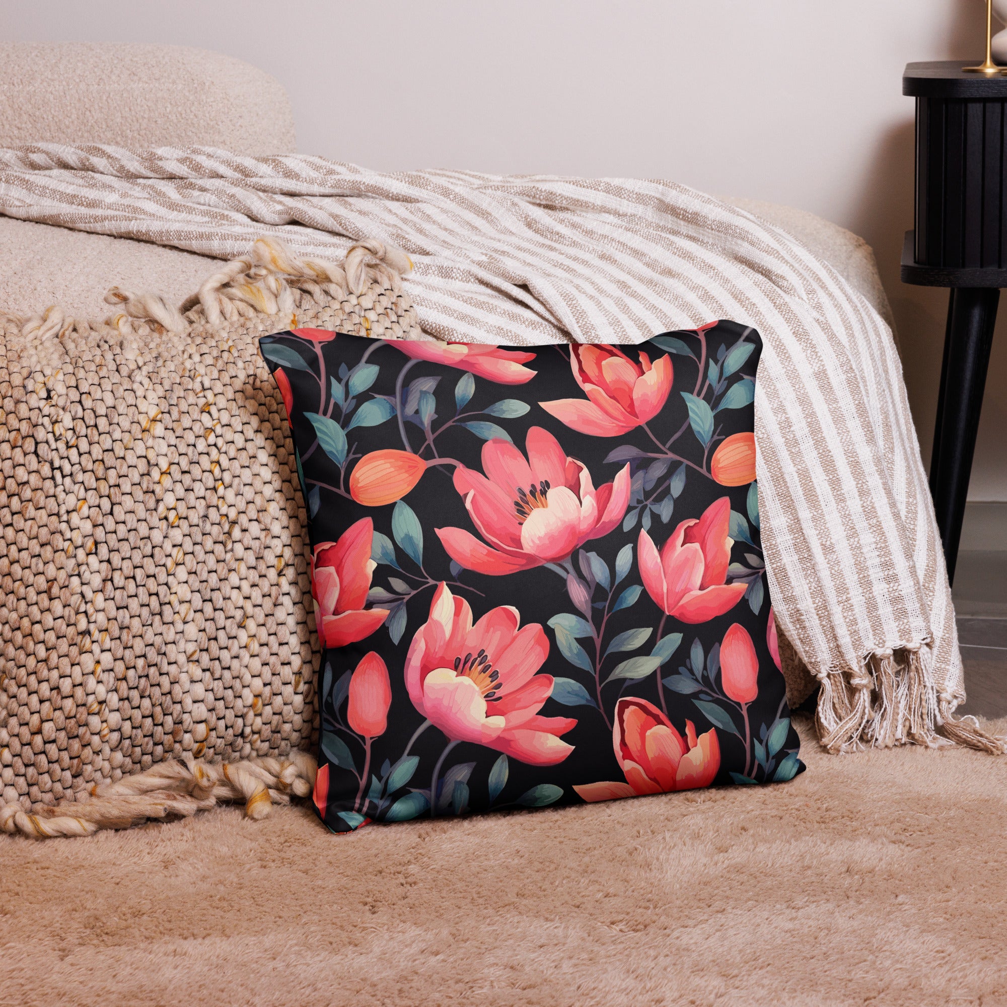 Decorative pillow featuring vibrant coral magnolia flowers on a black background, placed on a textured beige throw.