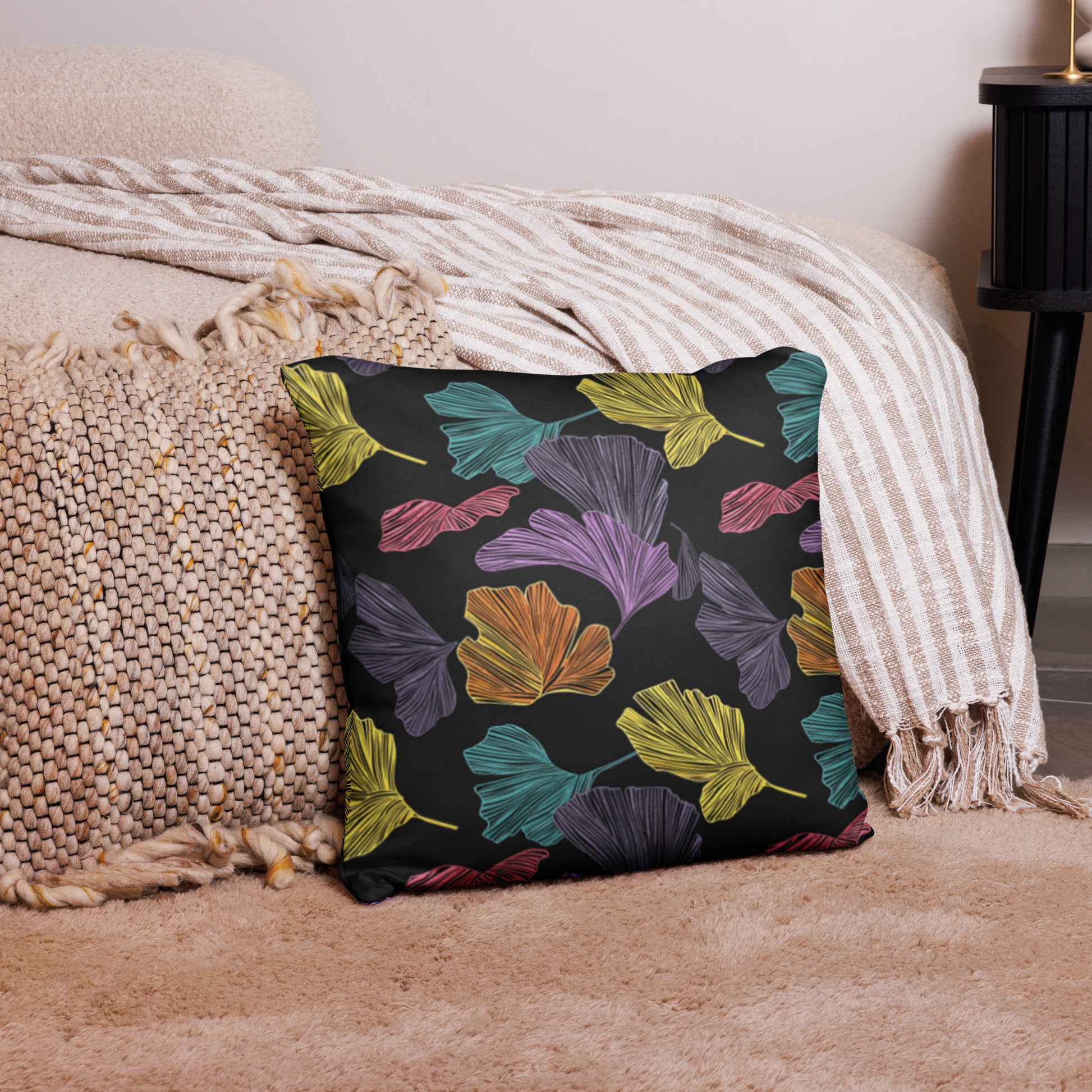 Holiday themed pillow with vibrant ginkgo leaf pattern in shades of purple, teal, orange, and yellow on a black knitted background