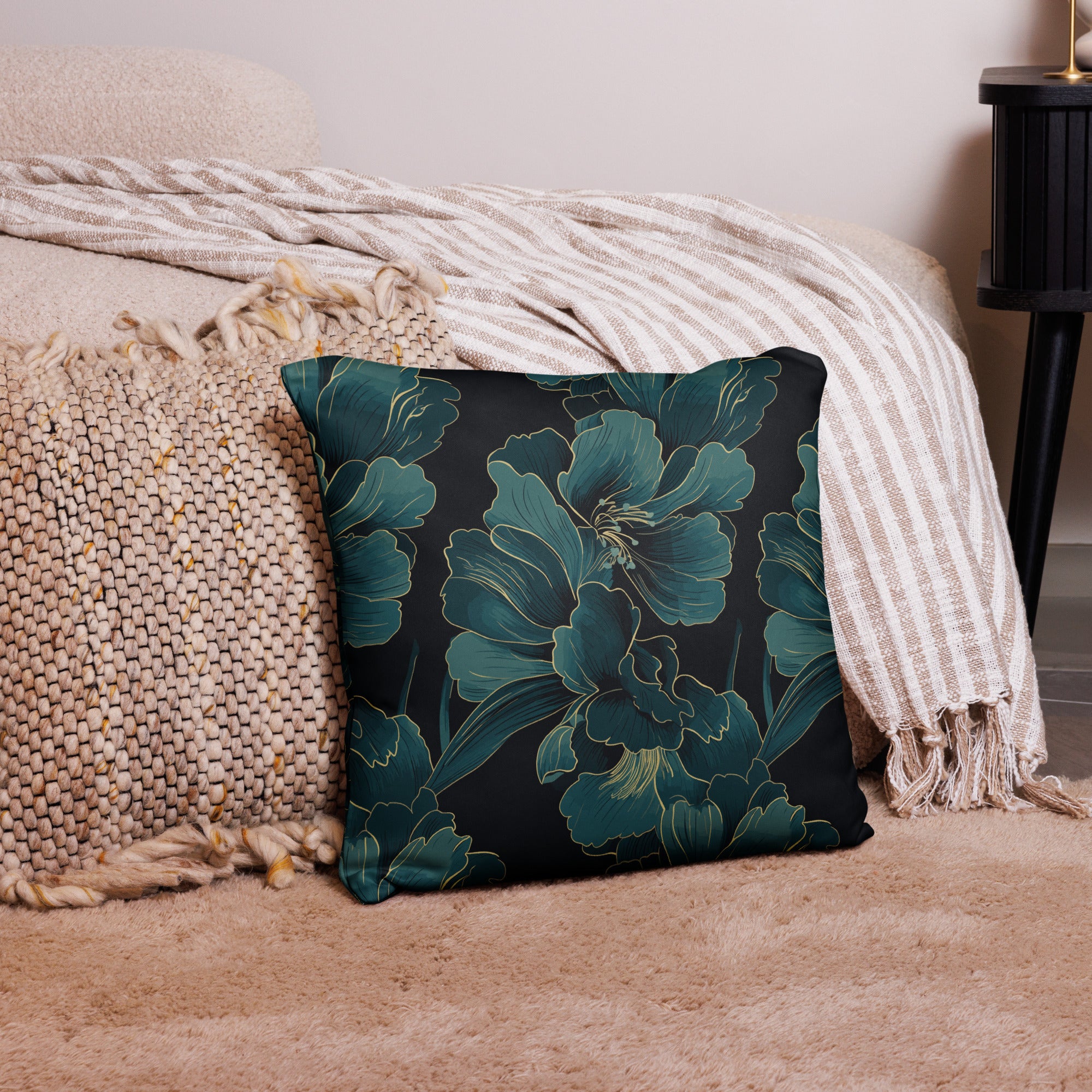 Square pillow with teal floral design on dark background, placed on cozy beige throw.