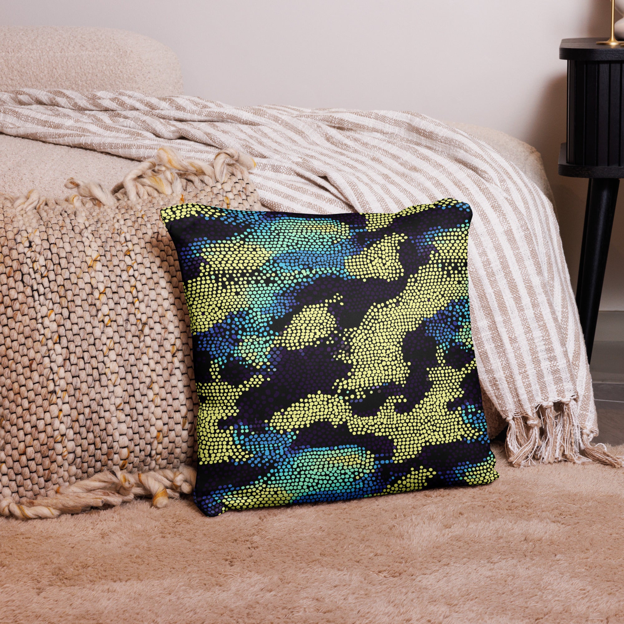 Dotted knitted throw pillow in shades of green, blue, and yellow on a cozy winter-themed setting with blankets and rugs.