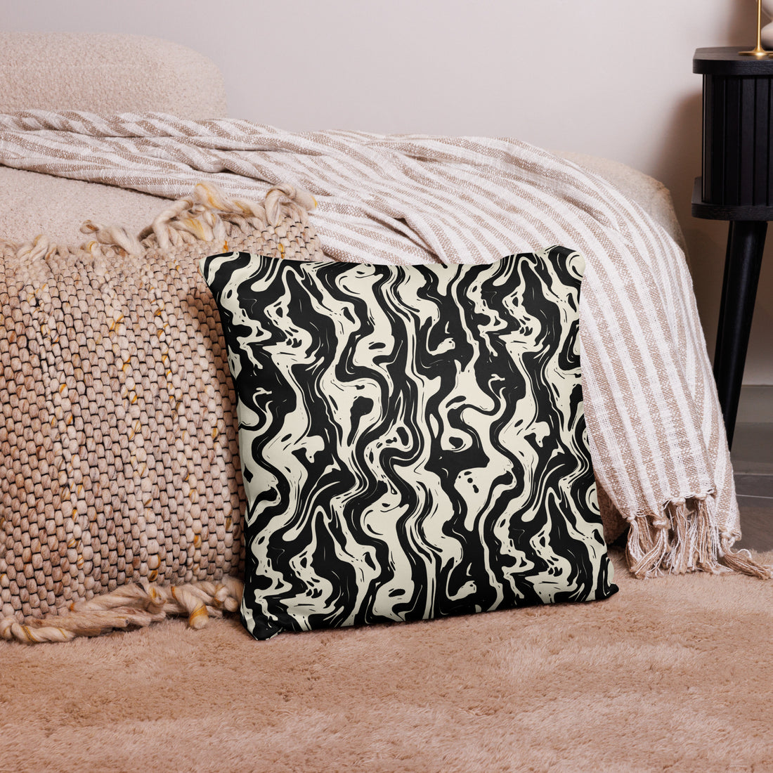 Black and white swirl patterned pillow placed on a beige rug with knitted blanket and decor items around.