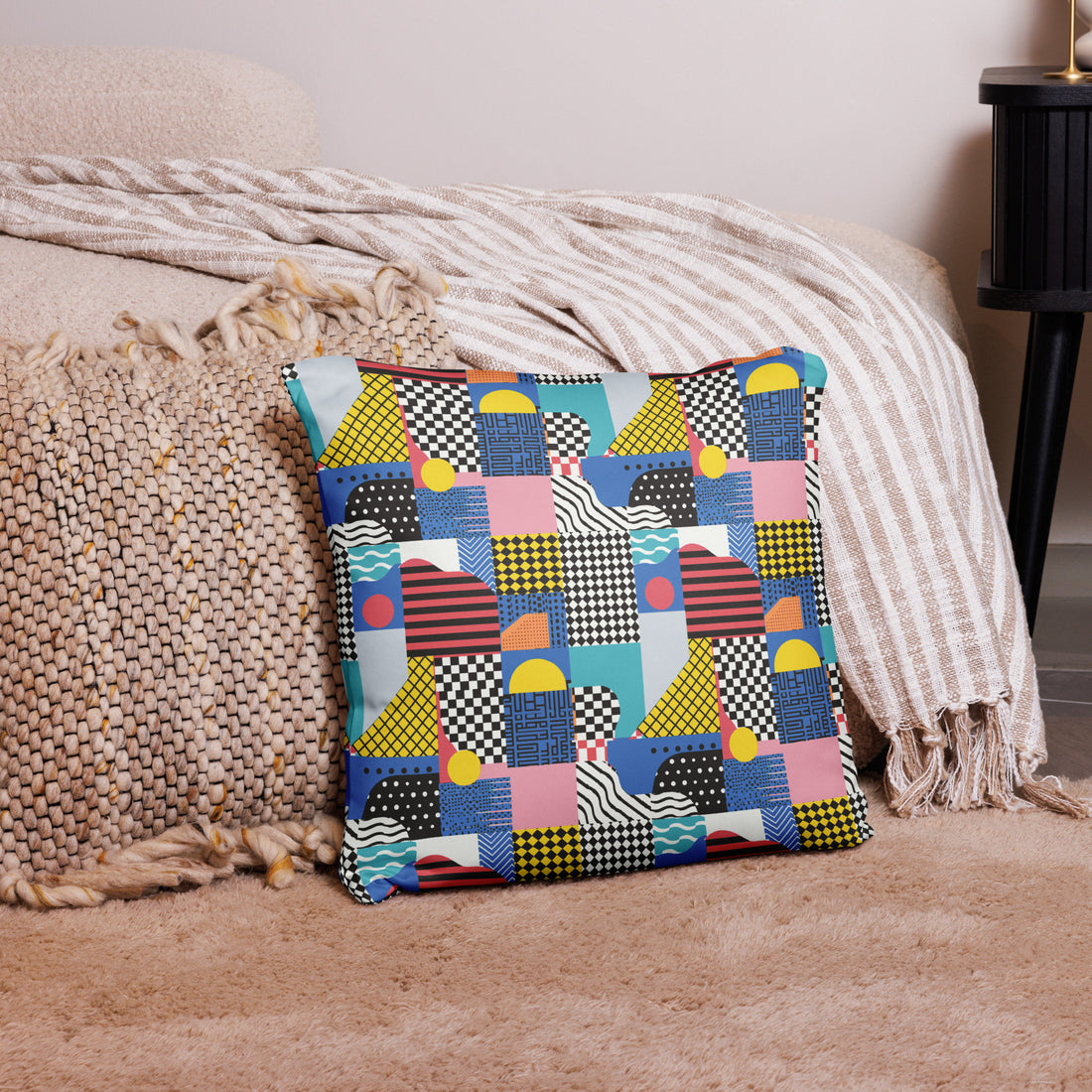 Colorful geometric patchwork pillow featuring vibrant shades of blue, yellow, pink, and black, placed on a textured couch.