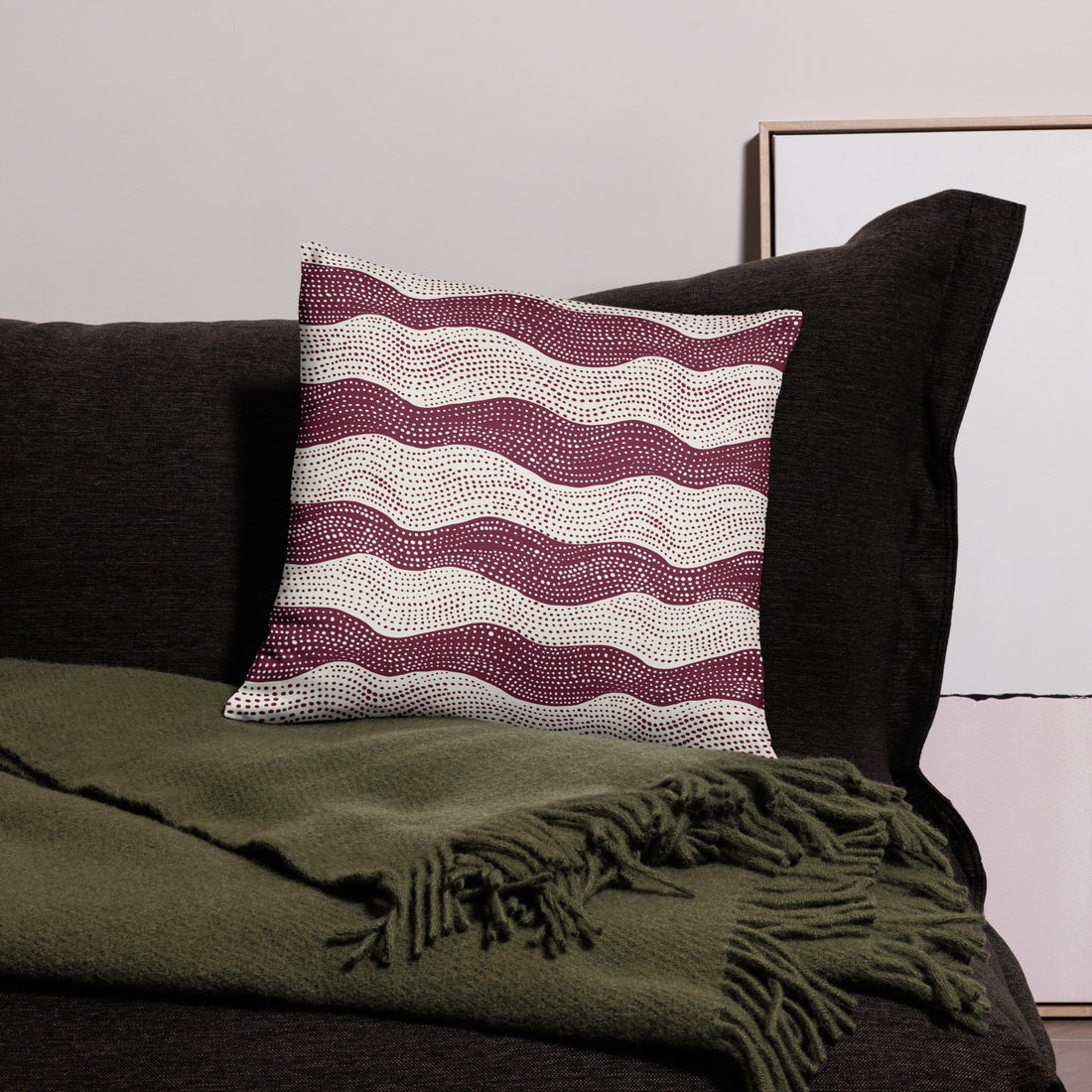 Knitted pillow with plum wave pattern, displayed on a dark sofa beside a green throw blanket.