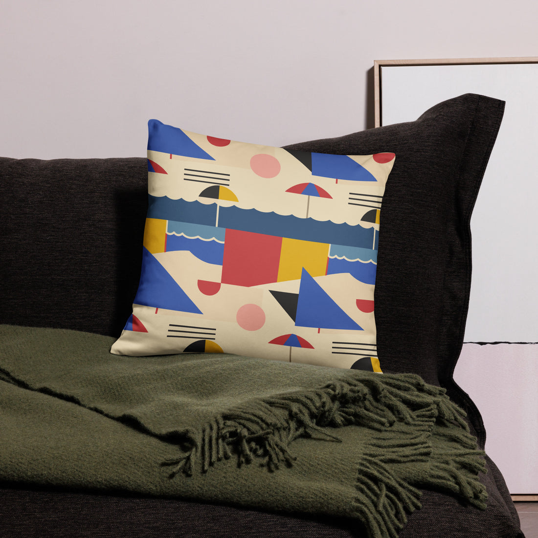 Decorative pillow with colorful geometric and beach umbrella design on a dark sofa with a green throw blanket.