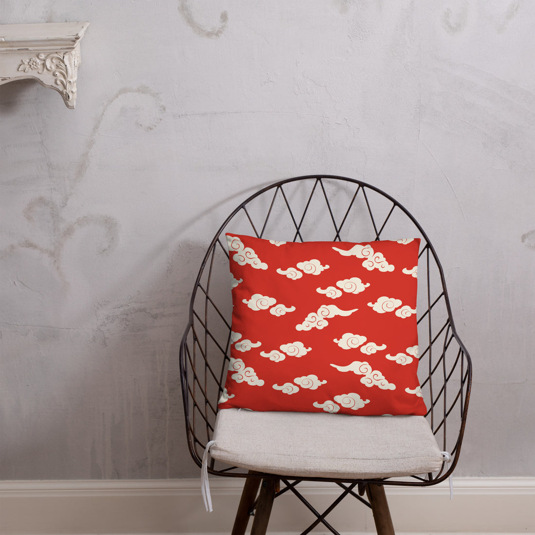 Red accent pillow with whimsical white cloud pattern on a grey textured wall background, nestled on a dark blue blanket.