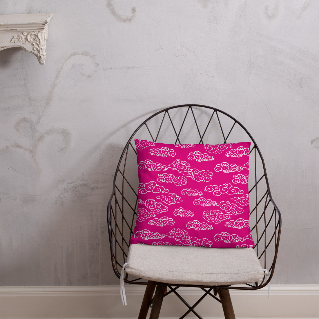 Festive Pink Cloud Knitted Accent Pillow on a dark bedspread with a gray wall background