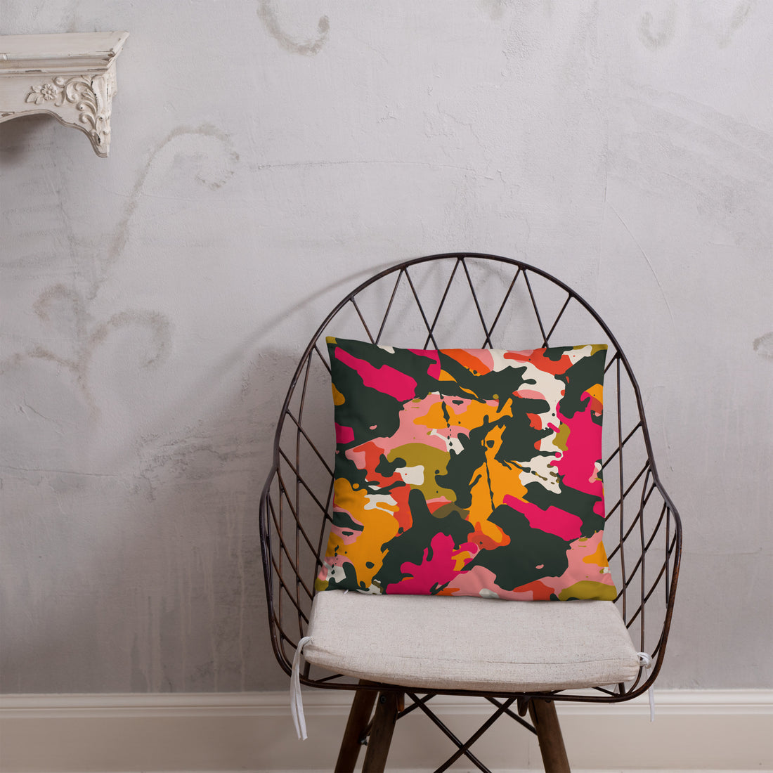 Accent pillow with a vibrant abstract camouflage design in pink, orange, green, and yellow on a soft fabric backdrop.