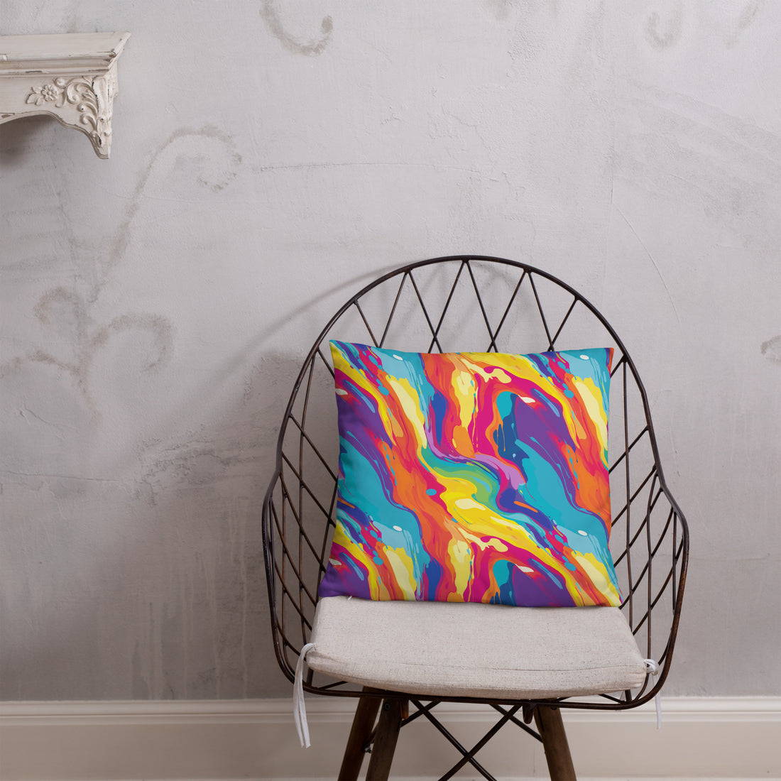 A vibrant knit pillow featuring a colorful abstract swirl design with bold blues, oranges, and yellows, placed against a textured wall backdrop.