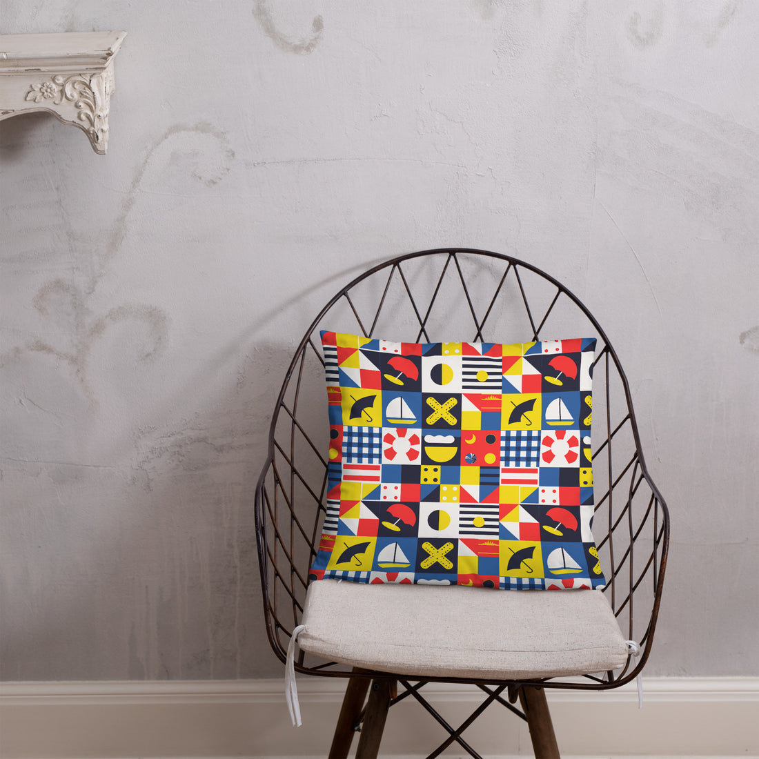 Colorful throw pillow with nautical and geometric flag designs in red, blue, yellow, and black on a cozy bedspread.