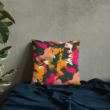 Accent pillow with a vibrant abstract camouflage design in pink, orange, green, and yellow on a soft fabric backdrop.