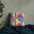 A vibrant knit pillow featuring a colorful abstract swirl design with bold blues, oranges, and yellows, placed against a textured wall backdrop.