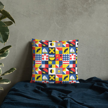 Colorful throw pillow with nautical and geometric flag designs in red, blue, yellow, and black on a cozy bedspread.