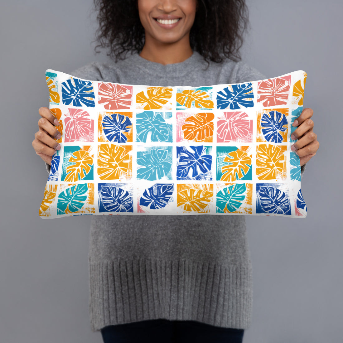 Close-up of a pillow with a colorful monstera leaf design featuring blue, orange, yellow, and pink colors on a knitted surface.