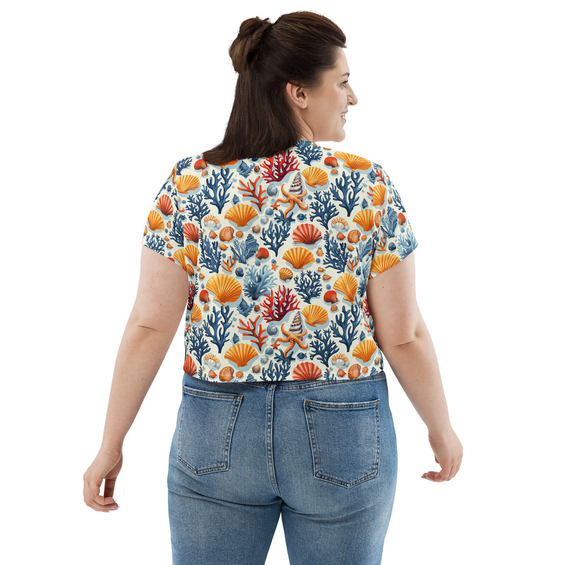 Woman wearing Oceanic Coral All-Over Print Crop Tee, featuring vibrant coral and seashell patterns with blue and orange hues.