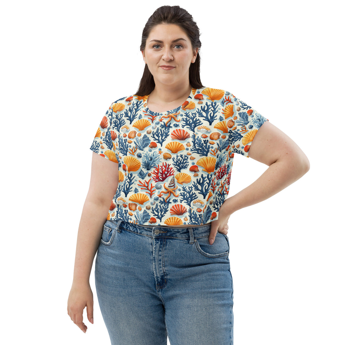 Woman wearing Oceanic Coral All-Over Print Crop Tee, featuring vibrant coral and seashell patterns with blue and orange hues.