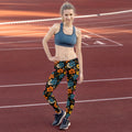 Woman wearing vibrant floral leggings with orange, teal, yellow flowers on a black background, standing on a running track.