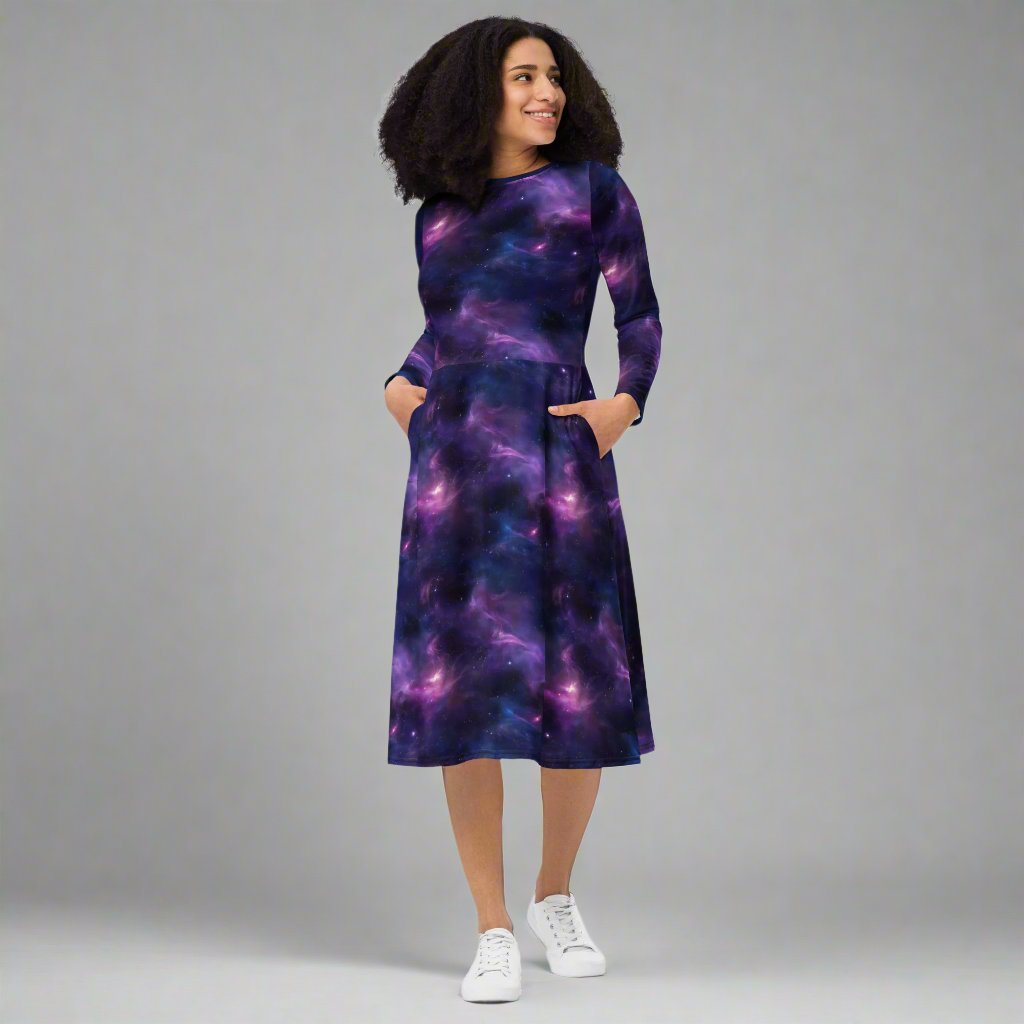 Woman wearing a long sleeve midi dress with an abstract galaxy design in purple and blue colors, featuring a fitted waist and pockets.