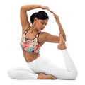 Woman wearing floral sports bra with vibrant coral, blue, and ivory flowers, performing yoga pose in white leggings.