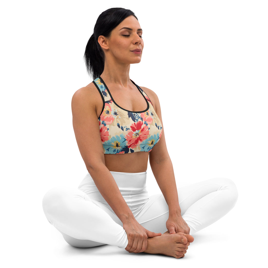 Woman wearing floral sports bra with vibrant coral, blue, and ivory flowers, performing yoga pose in white leggings.