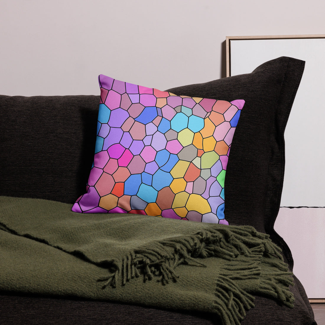 Colorful geometric premium pillow with a vibrant hexagonal pattern in shades of pink, blue, and yellow, displayed on a dark couch with a green throw blanket.