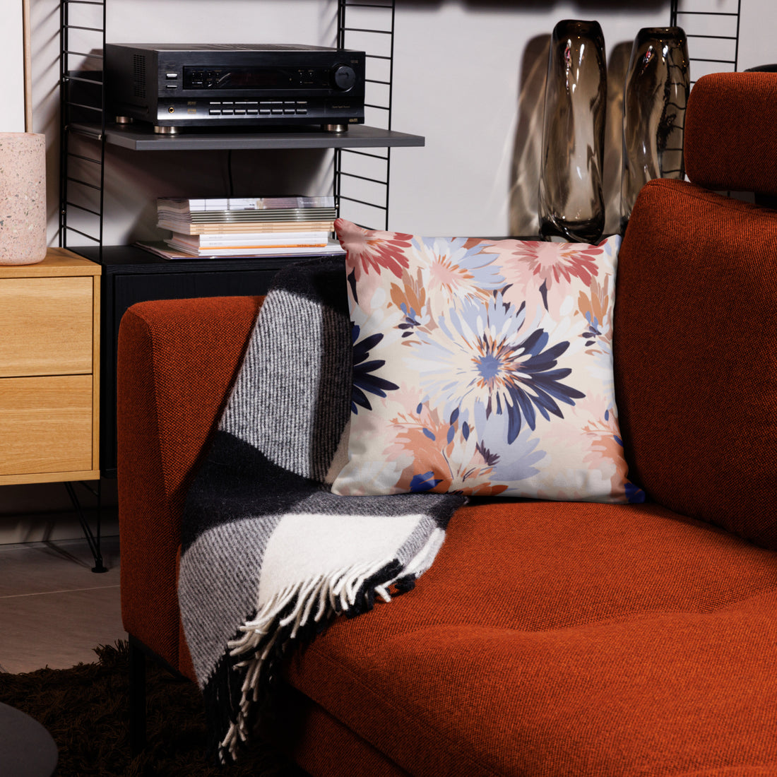 Floral throw pillow with blue and pink designs on a sofa next to a striped knit throw