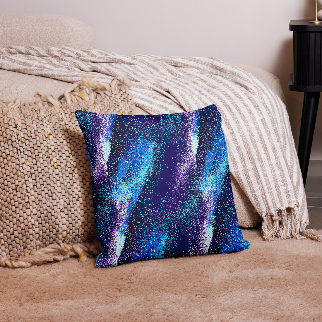 Knitted pillow with galaxy-inspired design in vibrant blues and purples on a cozy setting.