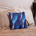 Knitted pillow with galaxy-inspired design in vibrant blues and purples on a cozy setting.