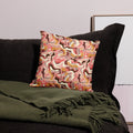 Pillow with abstract autumn camouflage design in pink, brown, and gold colors, placed on a dark sofa.