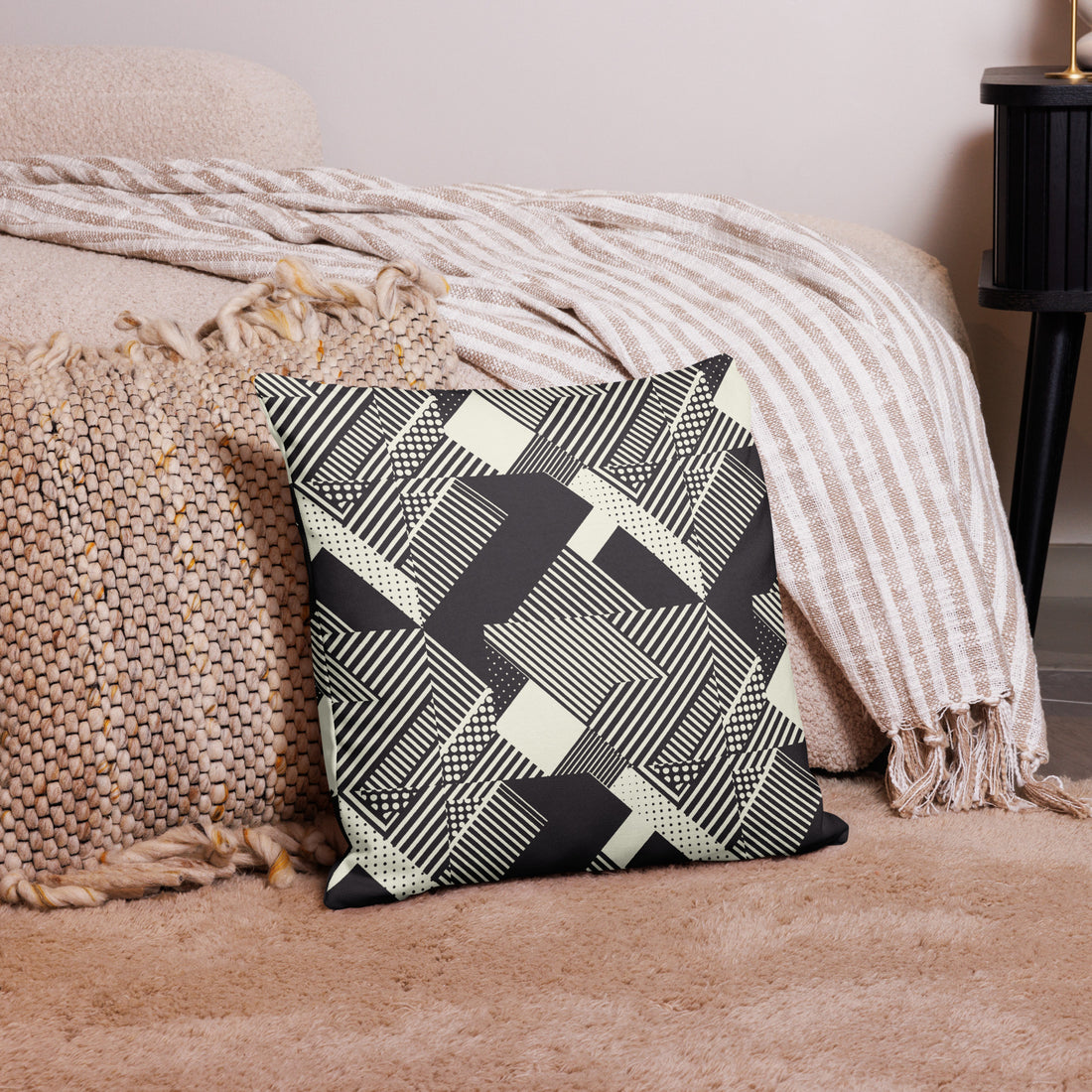 Decorative pillow with black and cream geometric knit design, placed on cozy beige carpet next to woven blankets.