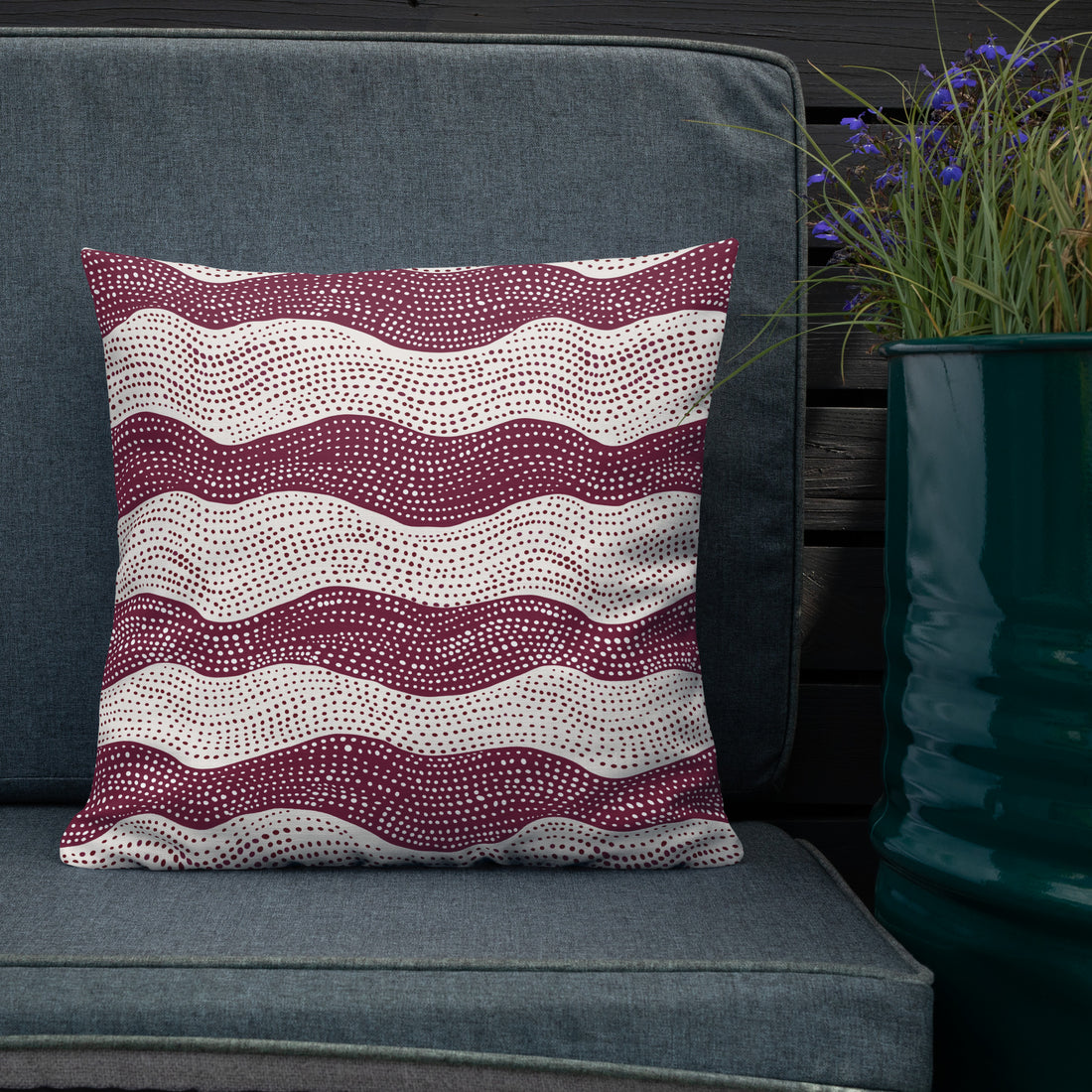 Burgundy knitted pillow with white wave patterns, cozy linen feel, placed on a chair next to a cup.