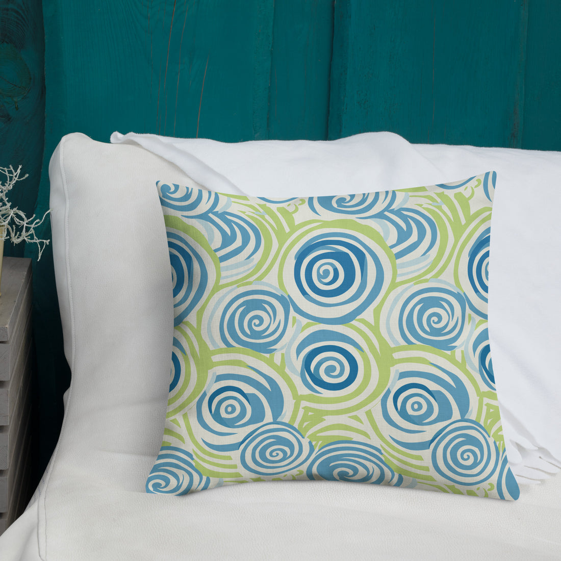 Elegant premium knitted pillow featuring a winter-inspired swirl pattern in shades of blue and green, placed on a dark blue bedspread.