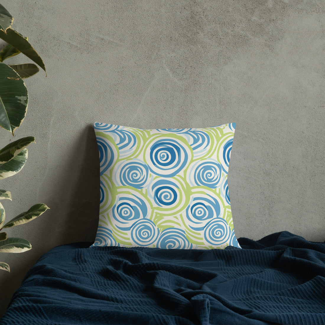 Elegant premium knitted pillow featuring a winter-inspired swirl pattern in shades of blue and green, placed on a dark blue bedspread.