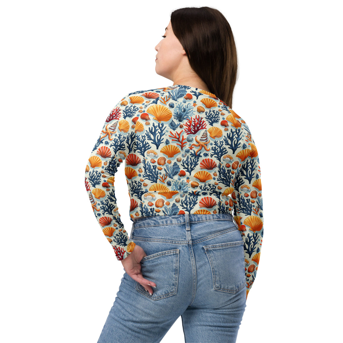 Woman wearing vibrant coral reef patterned crop top with colorful orange, blue, and red shell and coral motifs, paired with jeans.