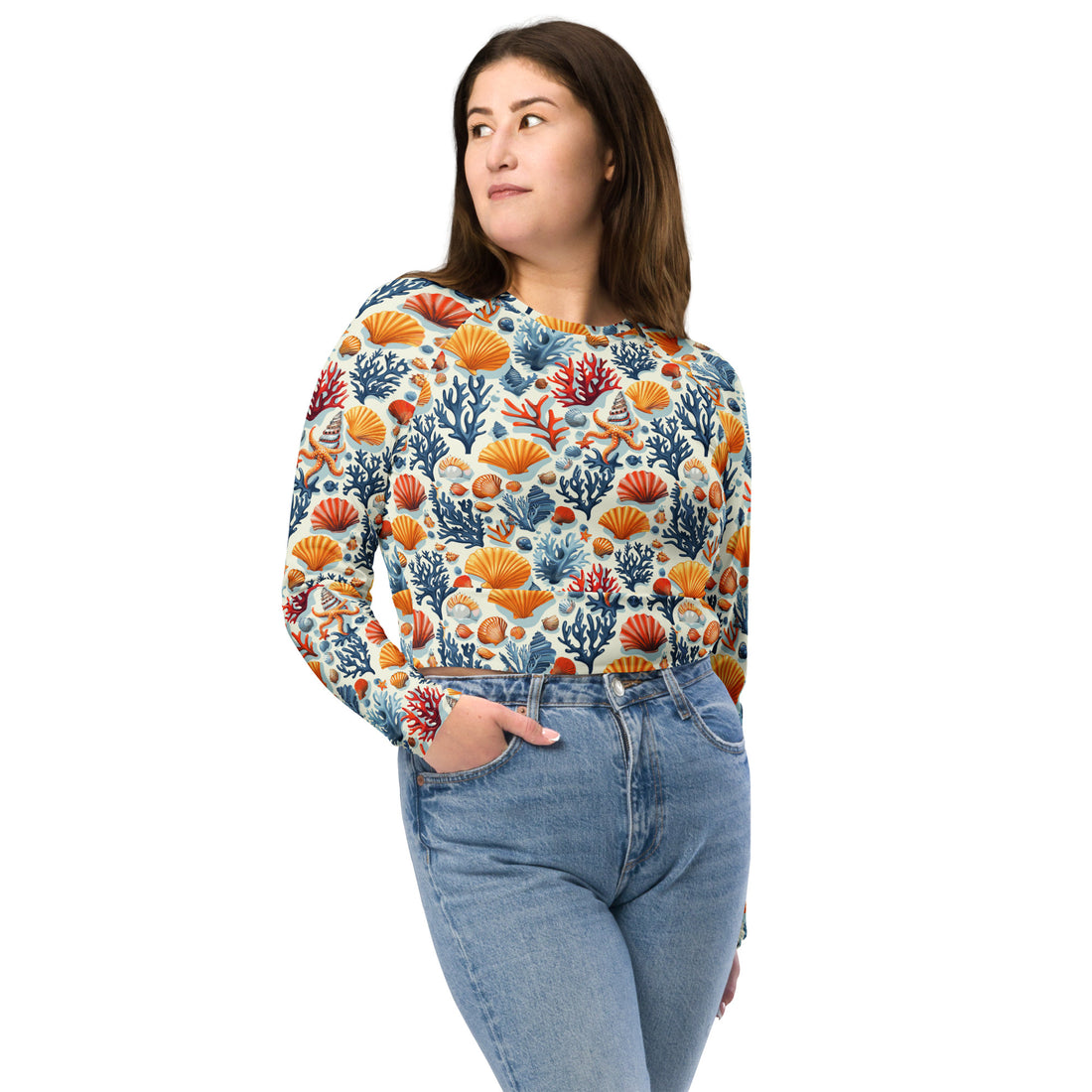 Woman wearing vibrant coral reef patterned crop top with colorful orange, blue, and red shell and coral motifs, paired with jeans.