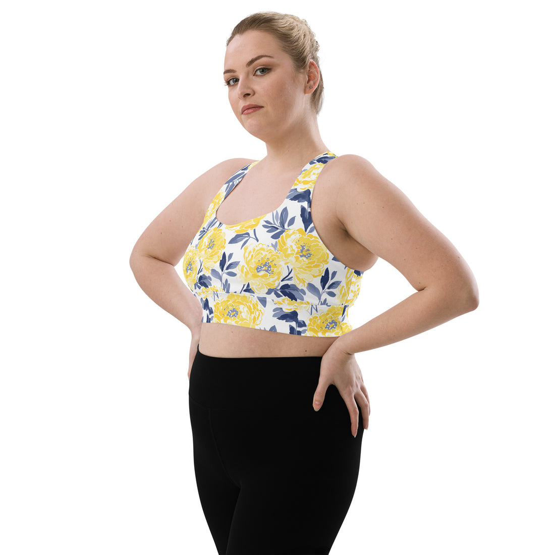 Woman wearing a longline sports bra with a bright yellow floral design on a white background, providing a vibrant and stylish look.