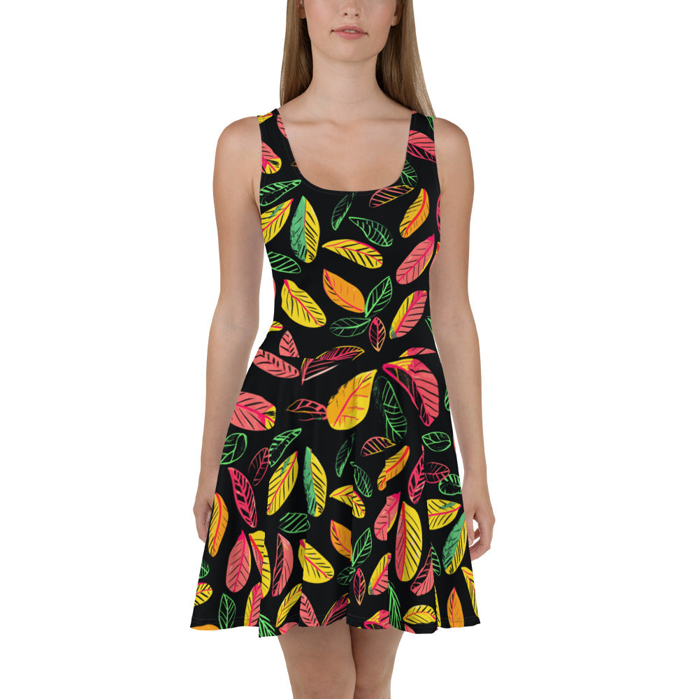 A sleeveless skater dress featuring a vibrant leaf print on a black background, designed for a flattering fit with a flared skirt.