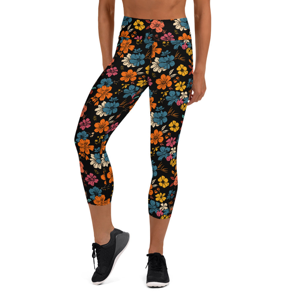 Woman wearing Floral Fusion Yoga Capri Leggings with colorful floral print in orange, blue, and yellow against a black background.