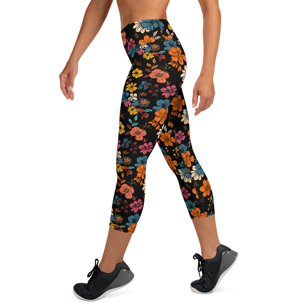 Woman wearing Floral Fusion Yoga Capri Leggings with colorful floral print in orange, blue, and yellow against a black background.