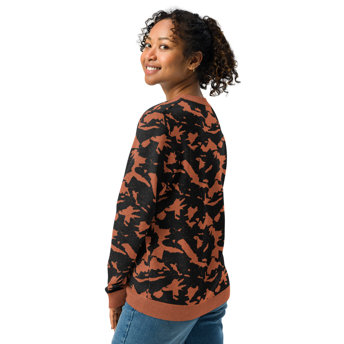 A woman smiling while wearing an autumn-inspired knitted crew neck sweater with a unique black and rust pattern.