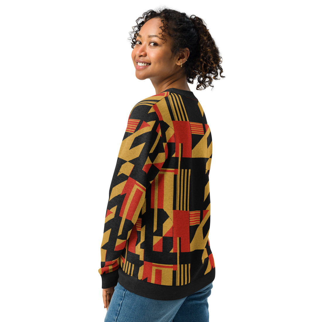 Woman wearing a knitted sweater featuring a bold geometric pattern in red, gold, and black, ideal for fall fashion trends.