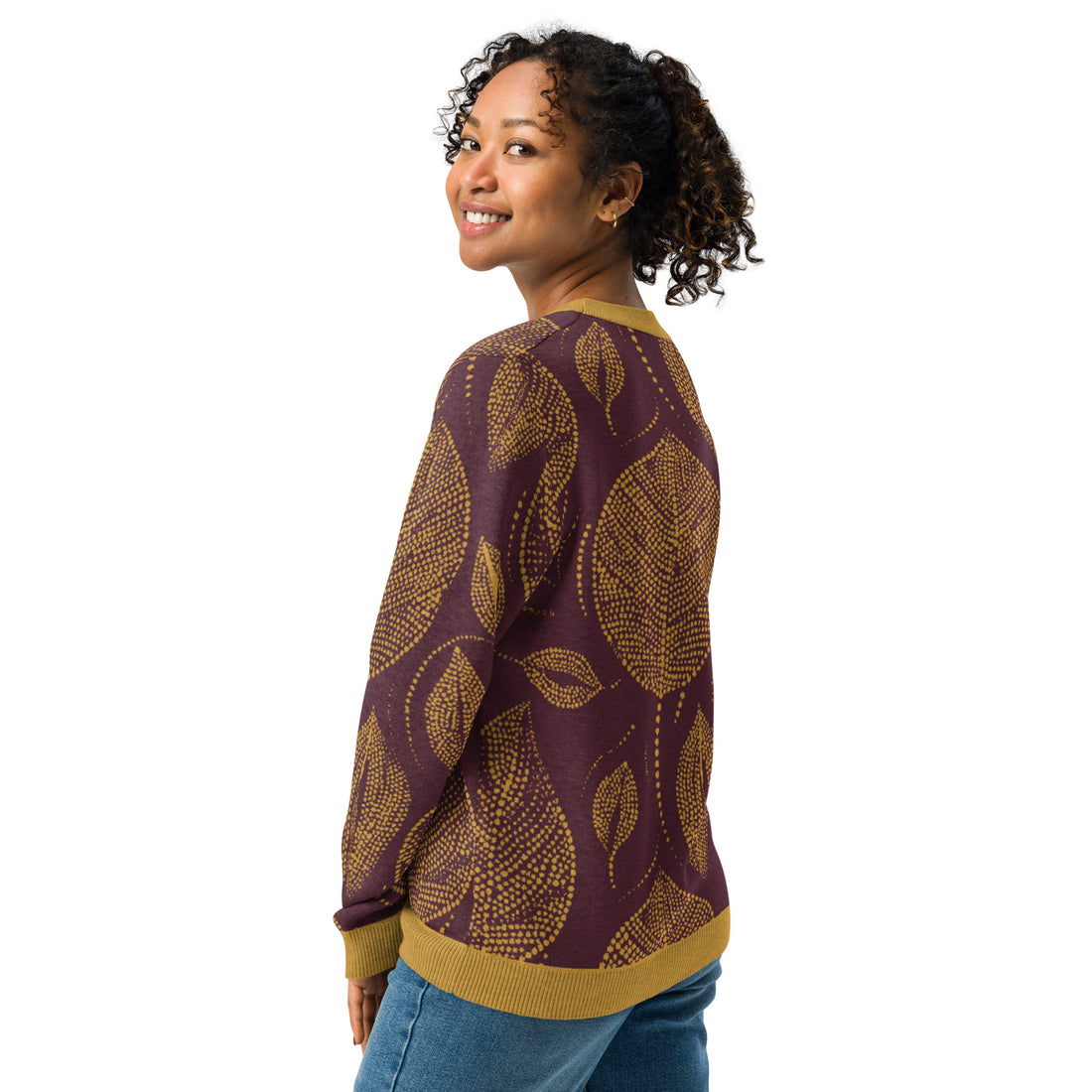 Woman wearing a maroon and mustard knitted sweater with a large autumn leaf pattern, showcasing a cozy and stylish fall design.